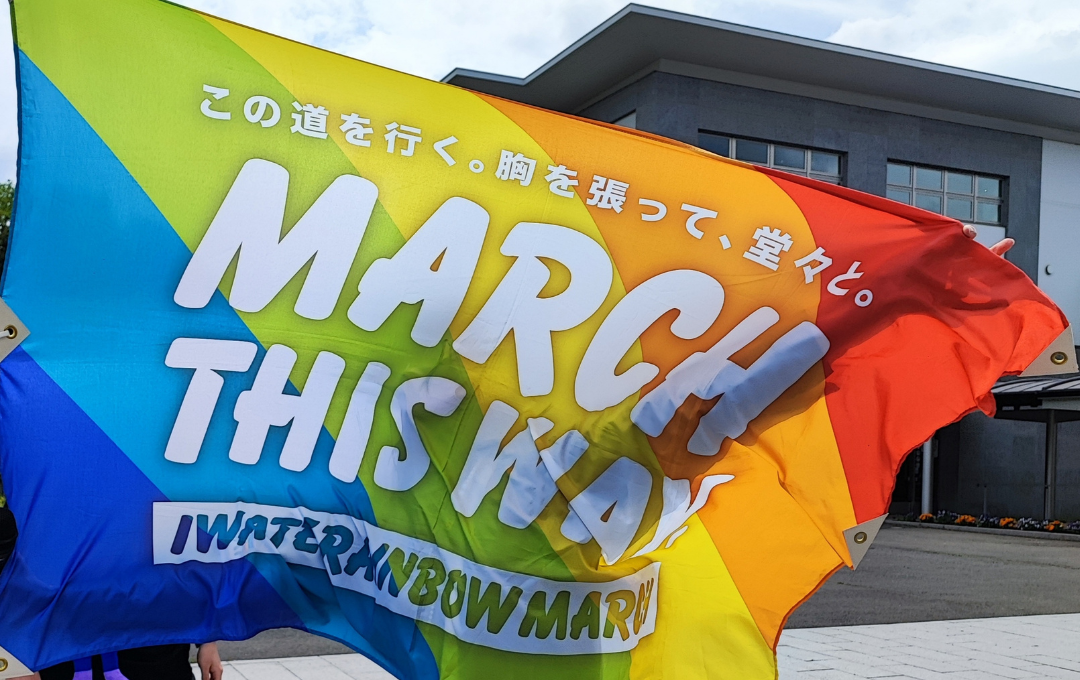 A photo of a rainbow-colored flag, associated with grassroots group Iwate Rainbow March, is held up by a person.